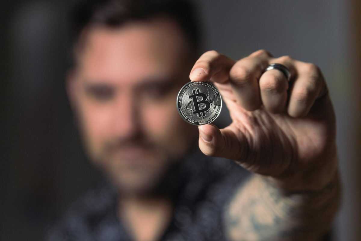 Adult male hand holding a Bitcoin, showcasing cryptocurrency focus indoors.