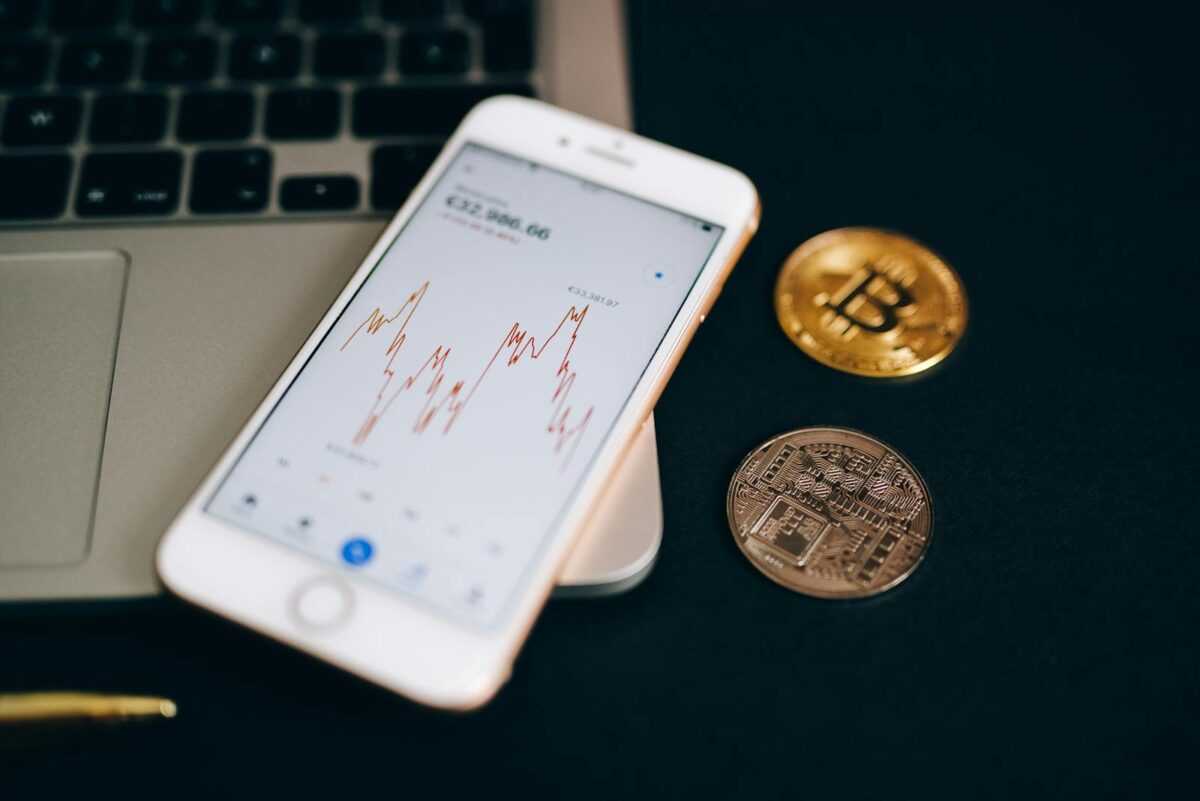 Close-up view of cryptocurrency coins and stock market graph on a smartphone screen.